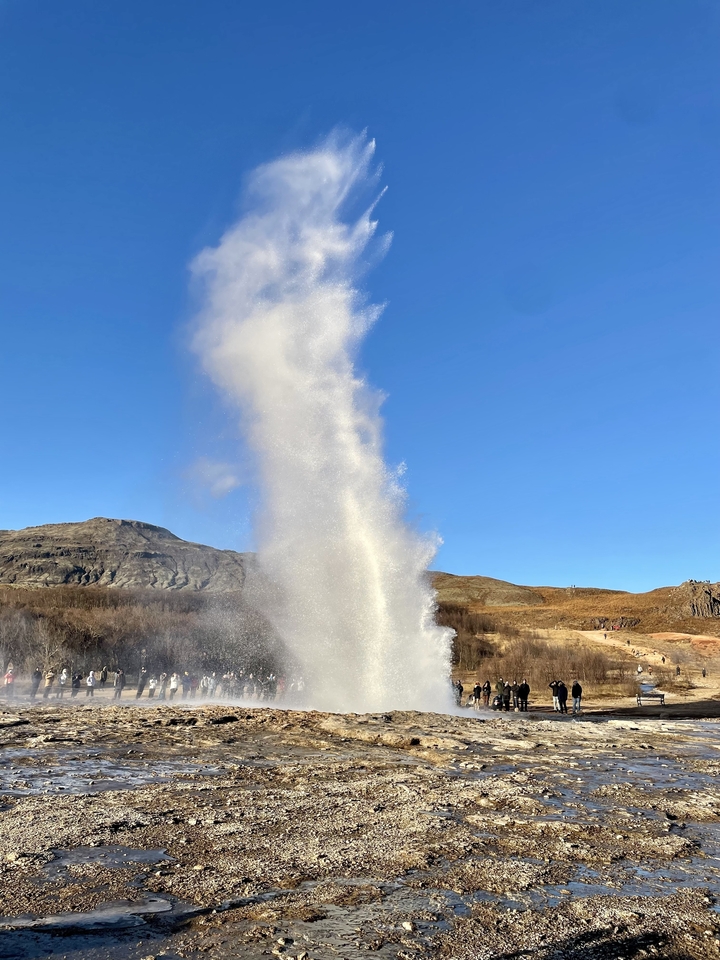 Un geyser en éruption dans un paysage rocheux sous un ciel bleu dégagé.