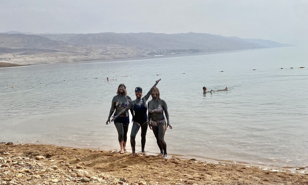 Trois personnes couvertes de boue se tenant près d'un lac.