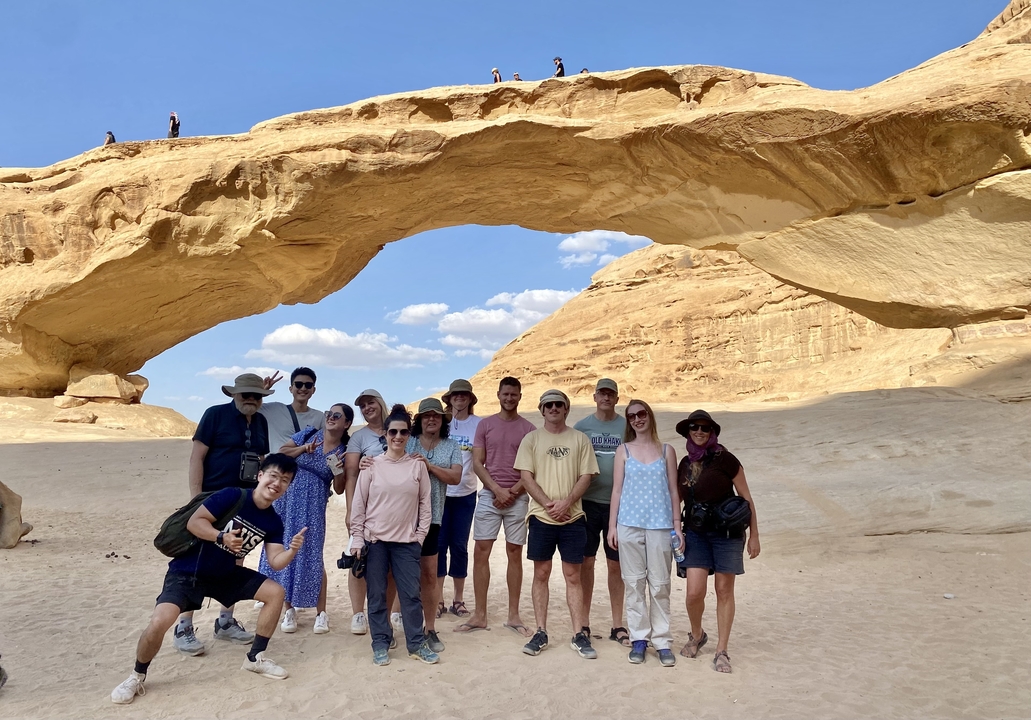 Groupe de personnes posant devant une grande arche de pierre.