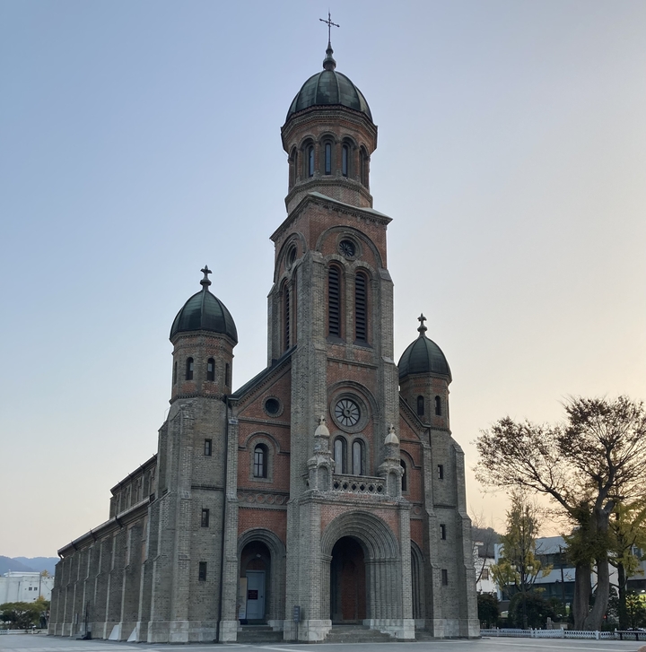 Une cathédrale en brique avec plusieurs dômes et une flèche sous un ciel clair.