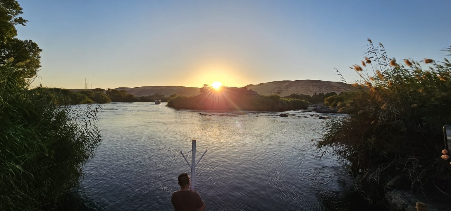 Vue calme de la rivière avec de hauts roseaux et des collines au loin.