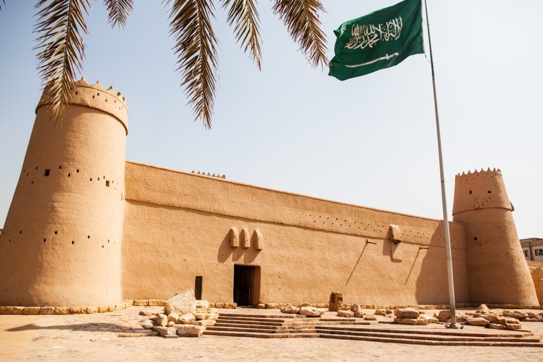 Un fort ancien avec un drapeau saoudien qui flotte devant.
