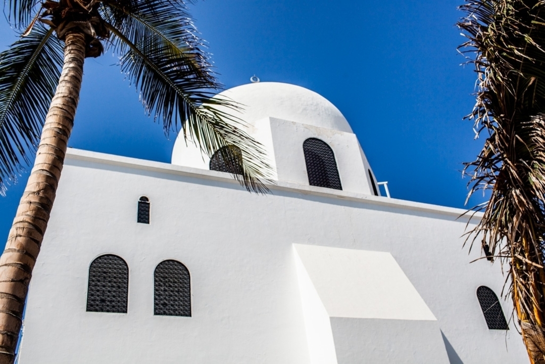 Une mosquée blanche avec des palmiers sous un ciel bleu éclatant.