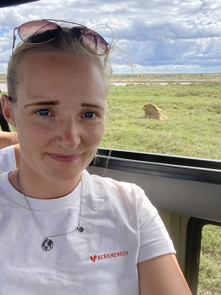 Une personne prenant un selfie avec un lion visible en arrière-plan.