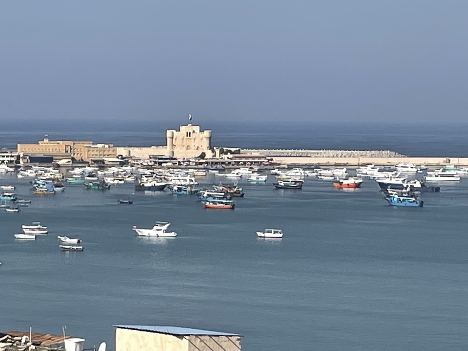 Un port avec des bateaux à l'ancre et une forteresse historique en arrière-plan.