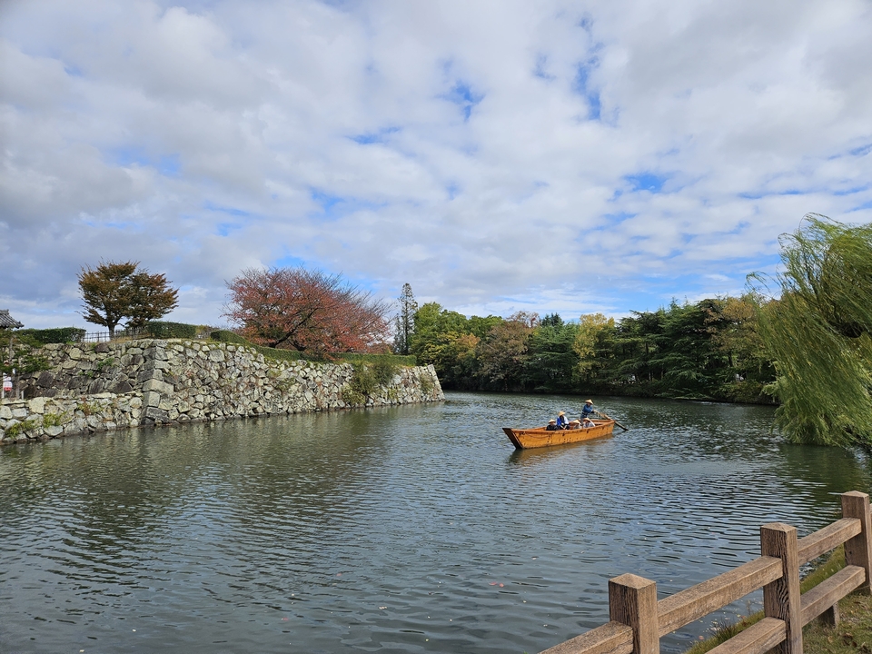 Des gens dans un bateau en bois sur des douves entourées d'arbres.