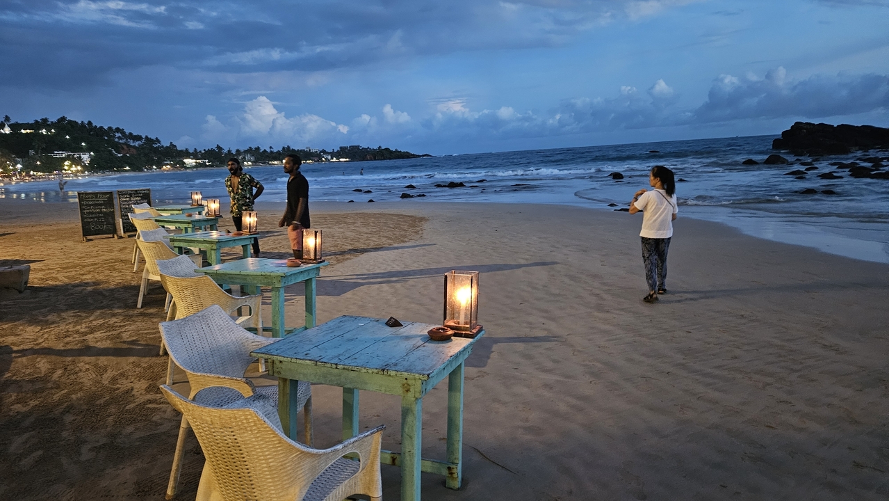 Vue sur le front de mer avec des tables dressées pour le repas et des personnes qui profitent du paysage.