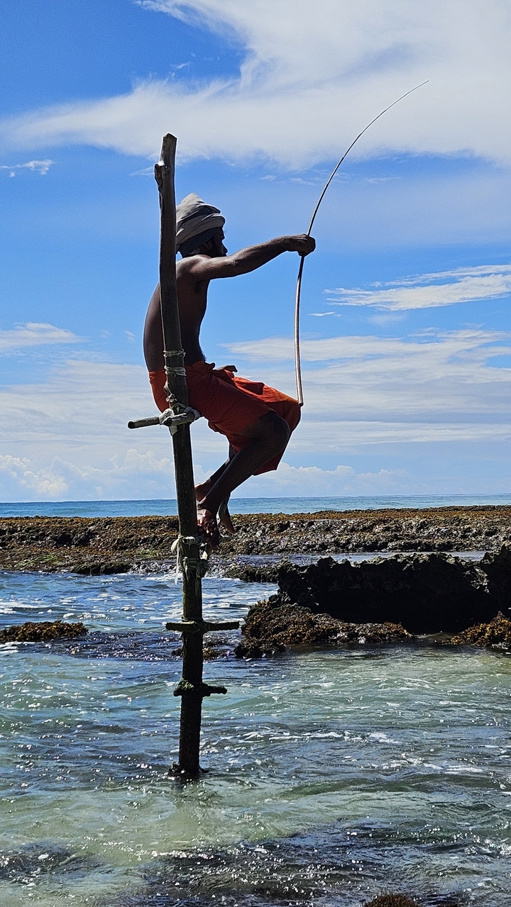 Pêcheur pratiquant la pêche sur échasses au-dessus de l'océan.