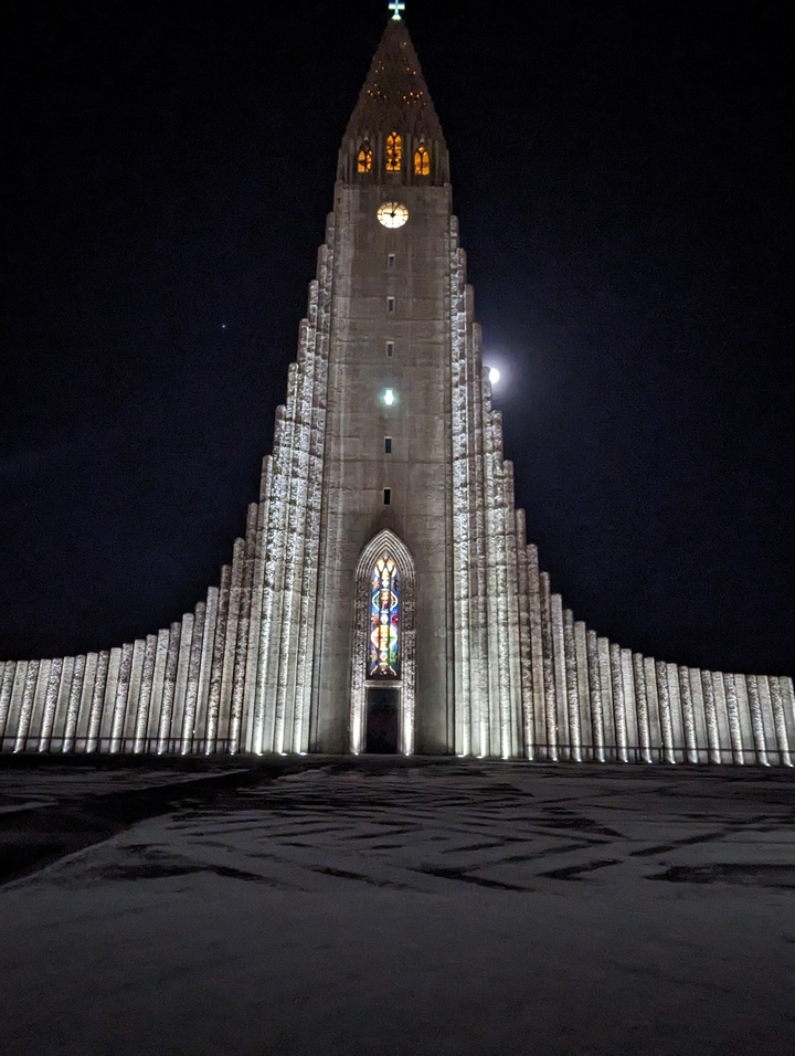 Vue nocturne de la Hallgrímskirkja illuminée avec la lune visible.