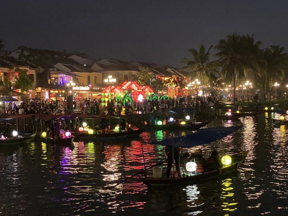 Scène de nuit au bord de la rivière avec des lumières colorées et des bateaux.