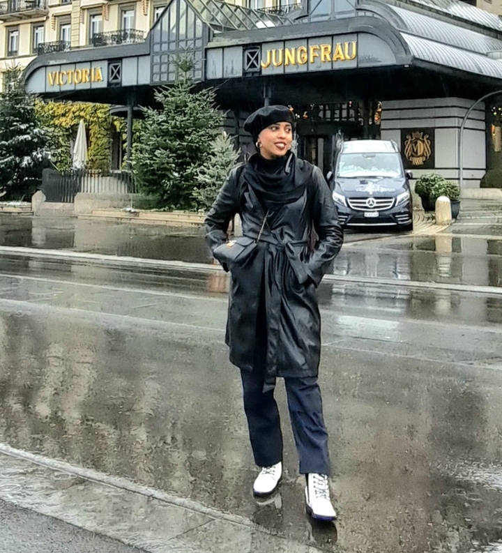 Eine Person in einem schwarzen Mantel, die auf einer nassen Straße steht.