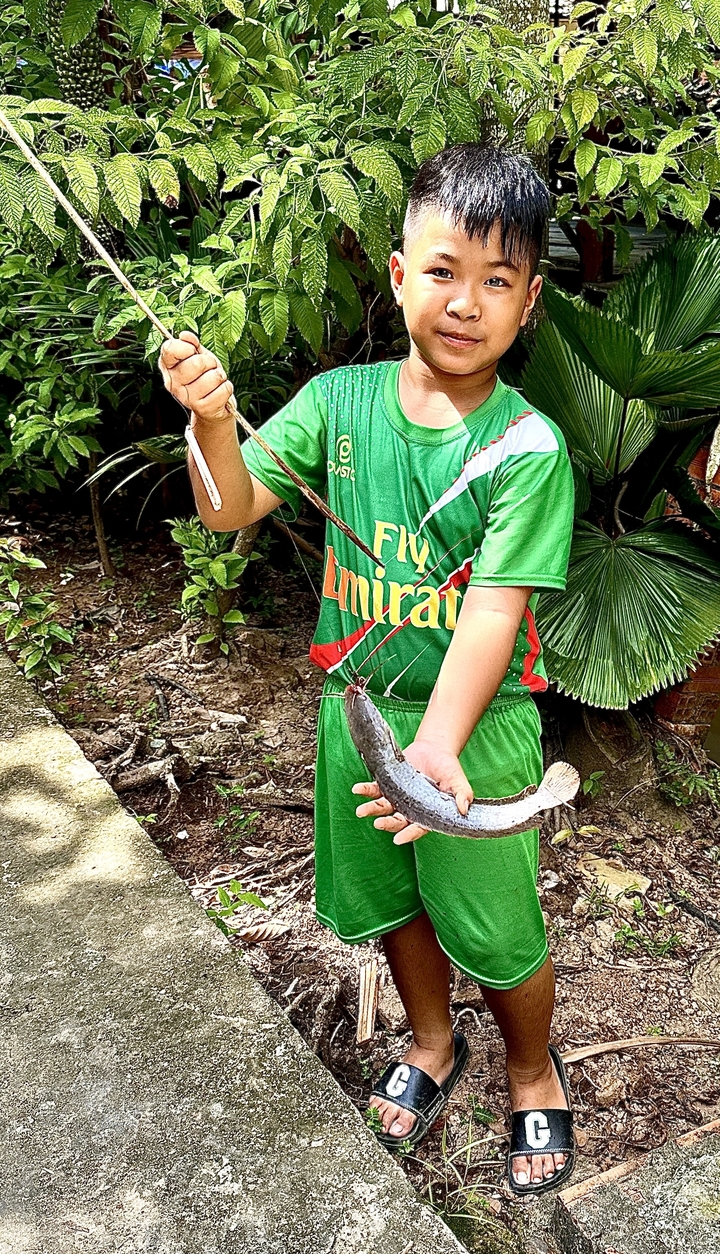 Enfant tenant un poisson avec de la verdure en arrière-plan.