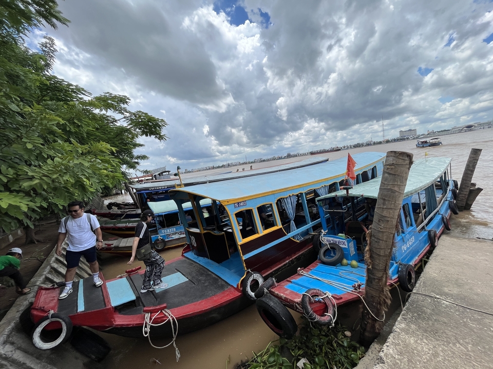 Des gens embarquent sur des bateaux au bord d'une rivière par temps nuageux.