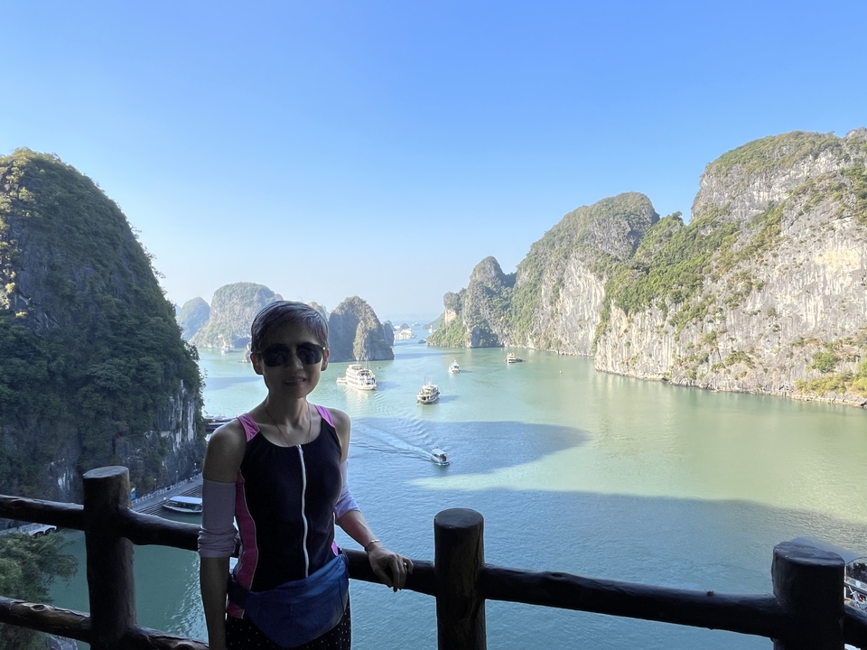 Femme debout devant la baie d'Halong avec des bateaux.