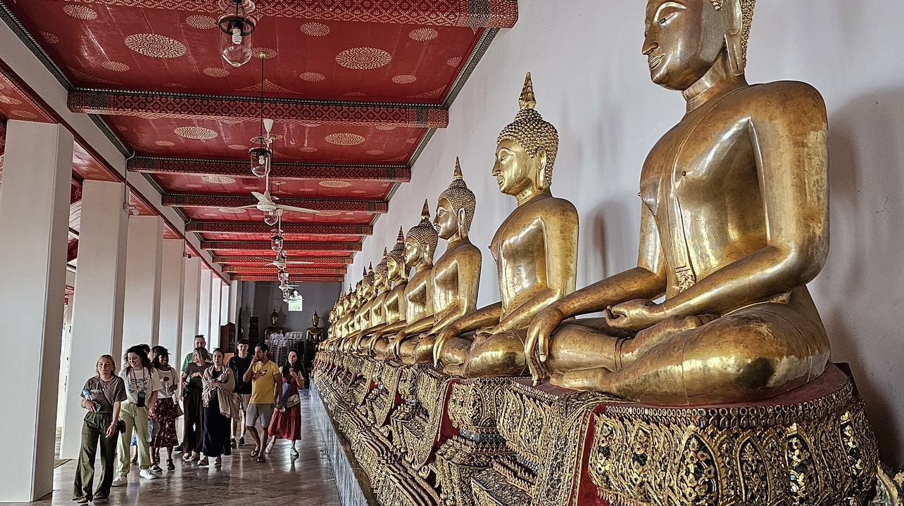 Rangée de statues dorées de Bouddha avec des touristes dans un temple.