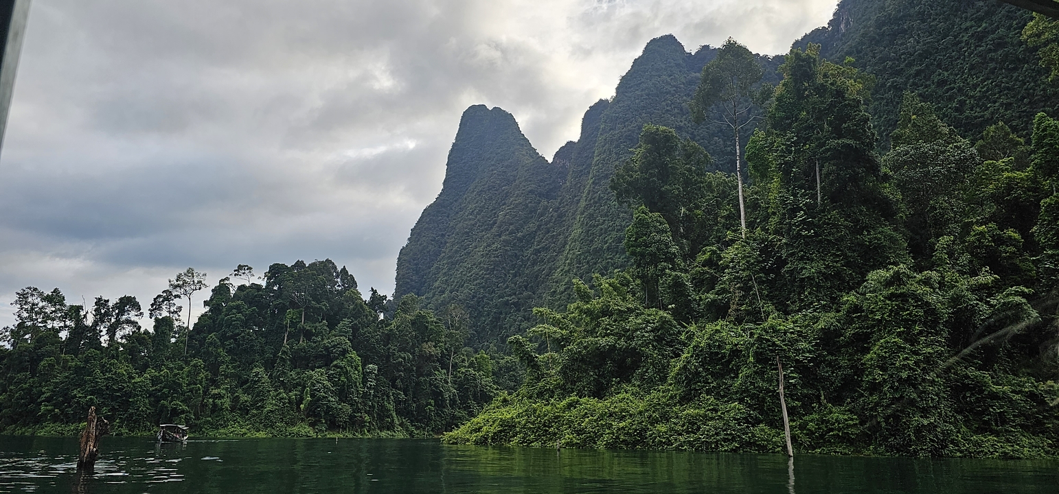 Montagnes vertes et eau réfléchissante sous un ciel nuageux.