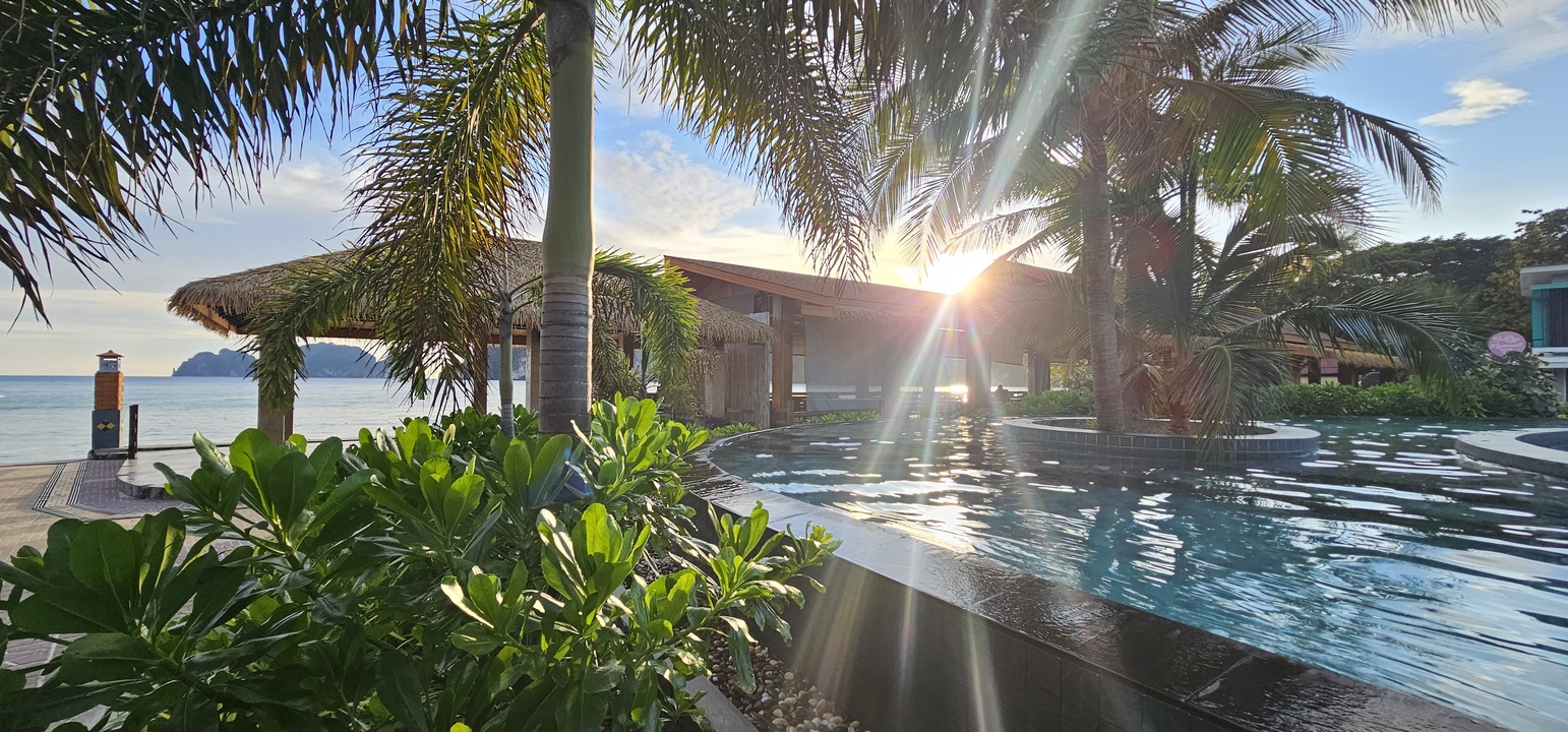 Station balnéaire avec piscine et palmiers au coucher du soleil.