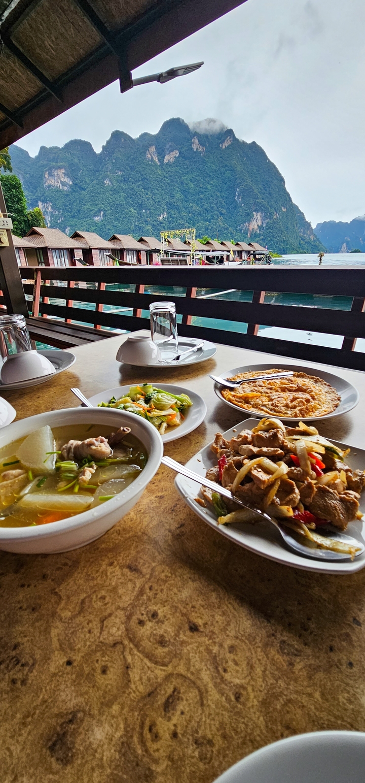 Table avec divers plats thaïlandais donnant sur un plan d'eau.