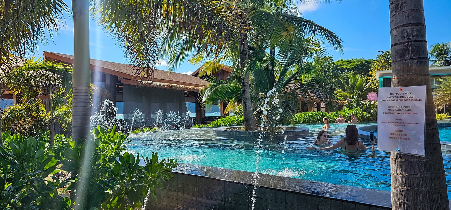 Zone de piscine de station balnéaire avec jeux d'eau et palmiers.