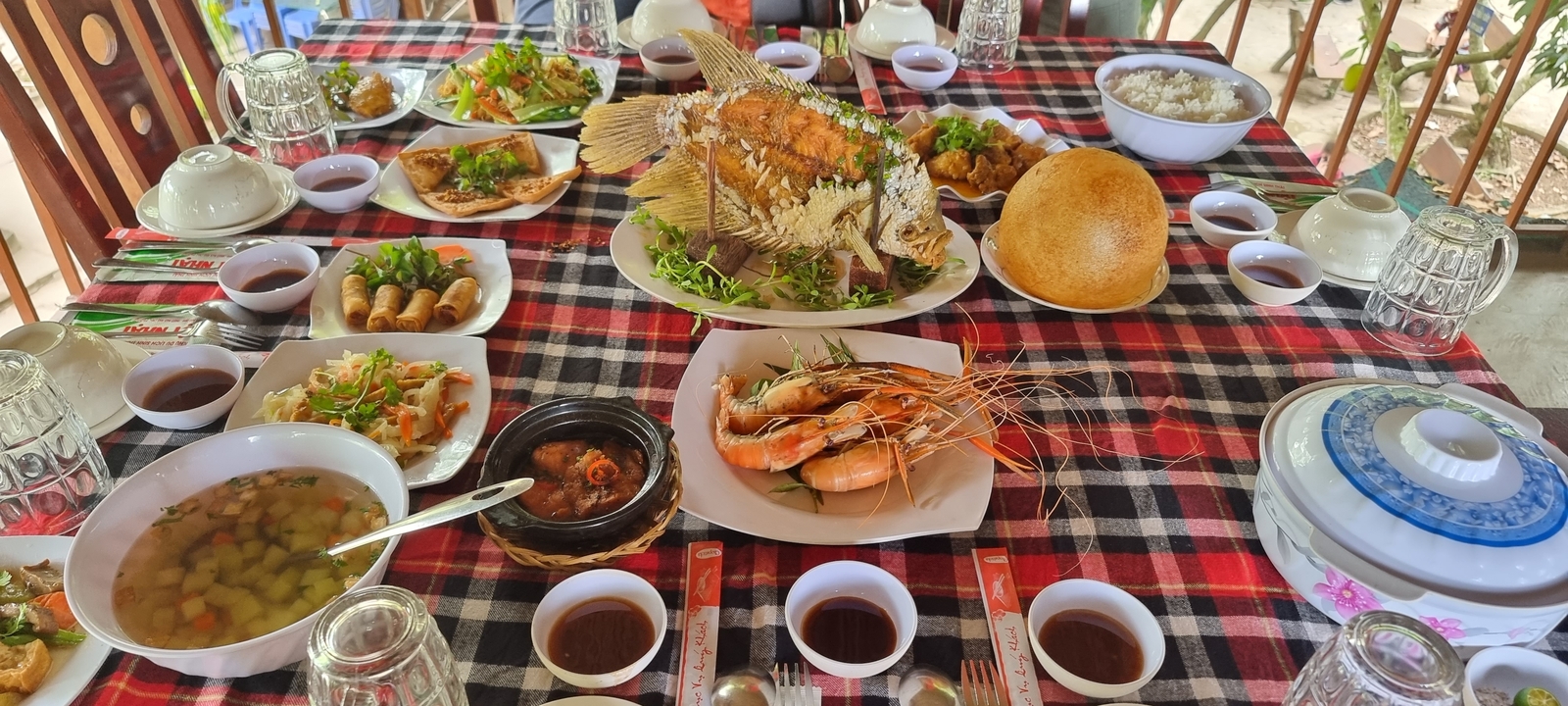 Une table remplie de plats vietnamiens traditionnels incluant un poisson entier et des crevettes.