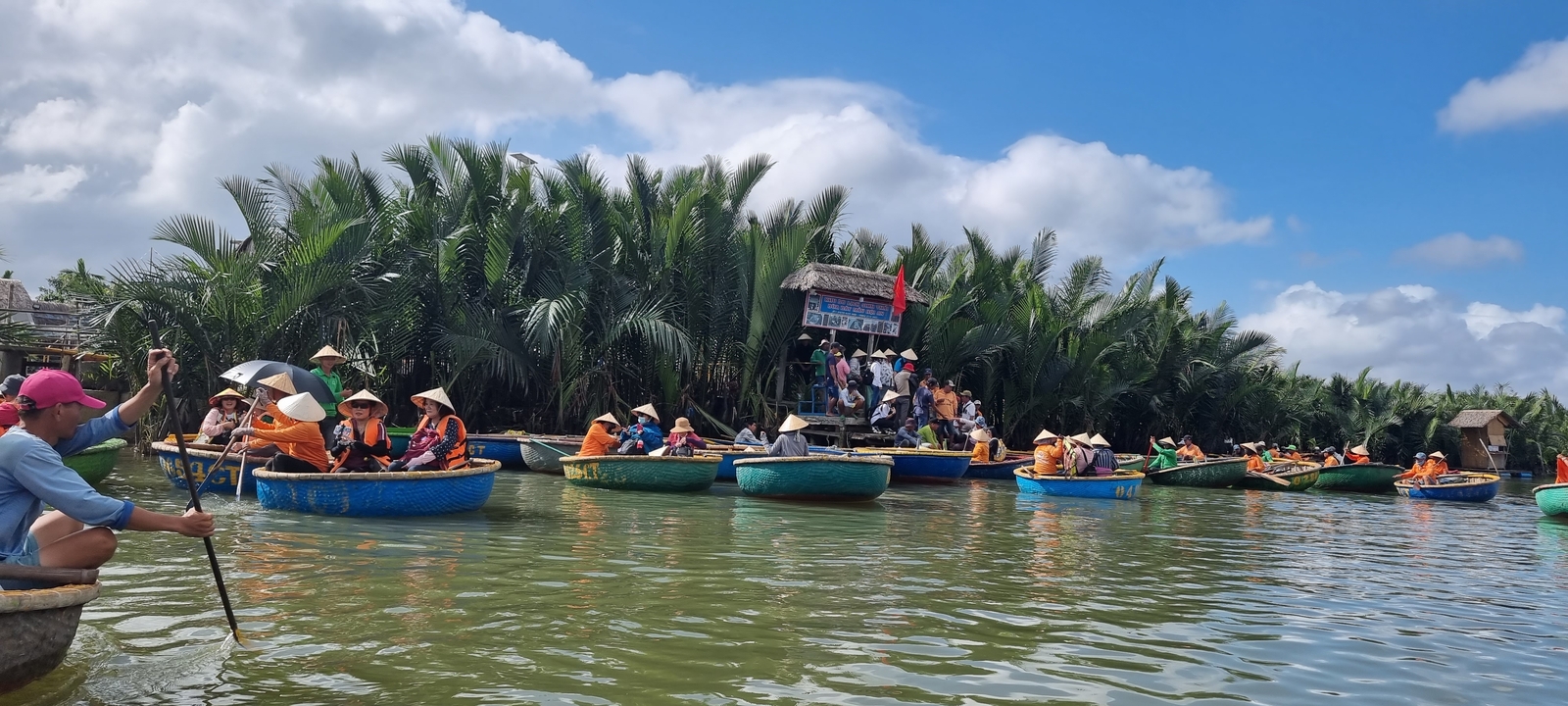 Un groupe de personnes portant des chapeaux traditionnels ramant dans des paniers colorés le long d'une rivière entourée d'une végétation luxuriante.