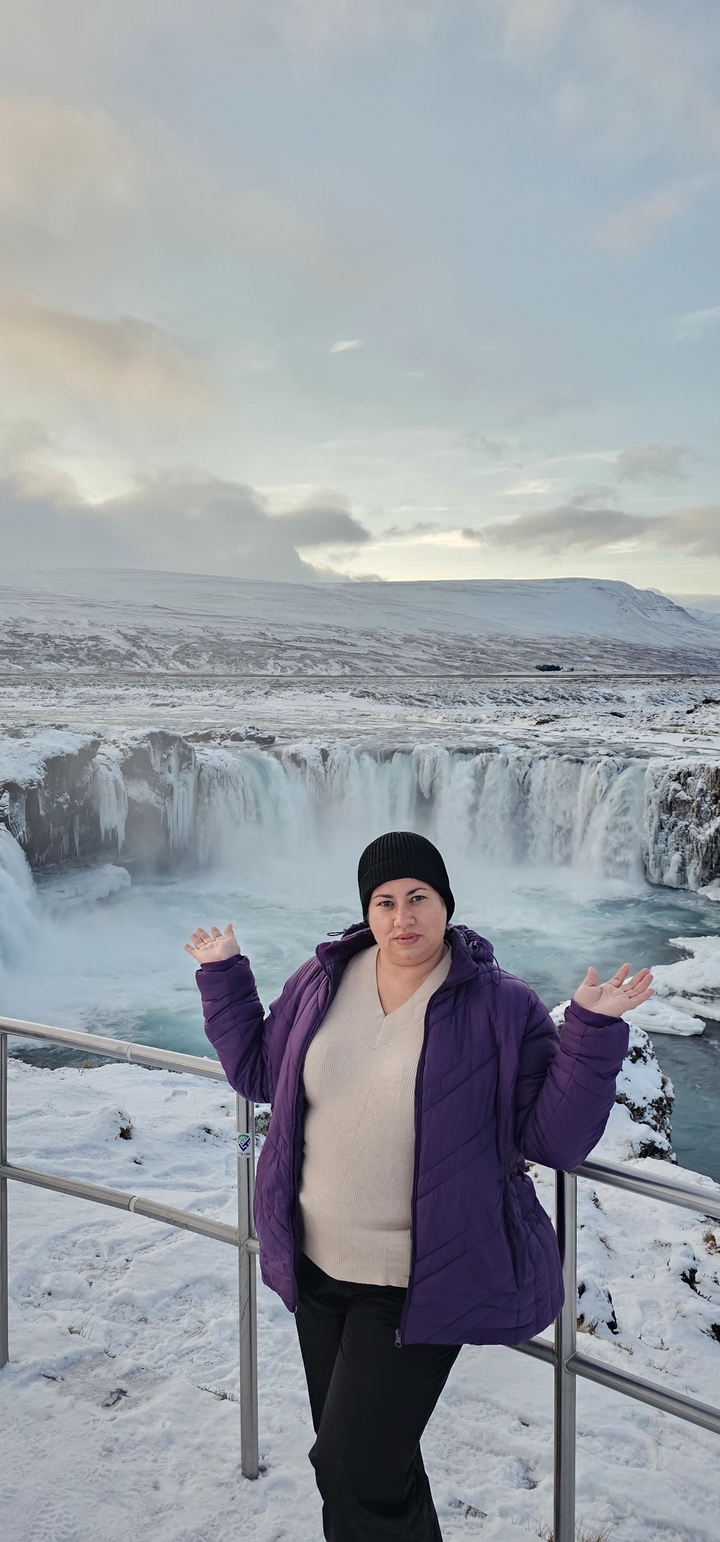 Personne posant devant une cascade enneigée.