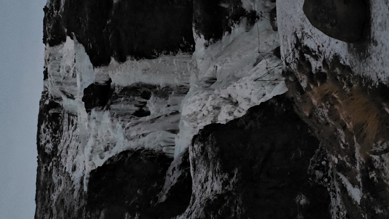 Falaise verticale sombre avec formations de glace.