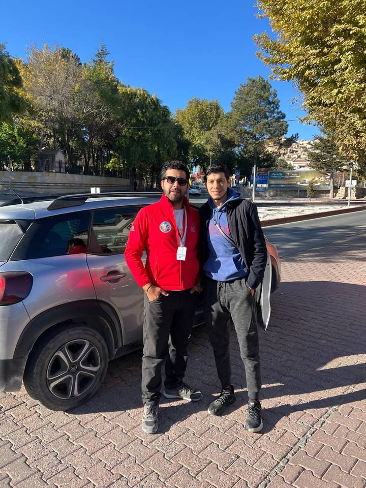 Deux personnes posant devant une voiture avec des arbres en arrière-plan.