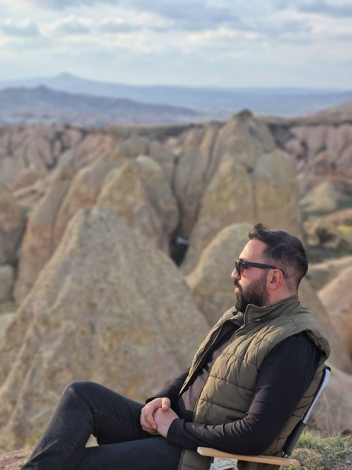 Un homme assis pensivement sur une colline rocheuse avec vue sur des formations rocheuses.
