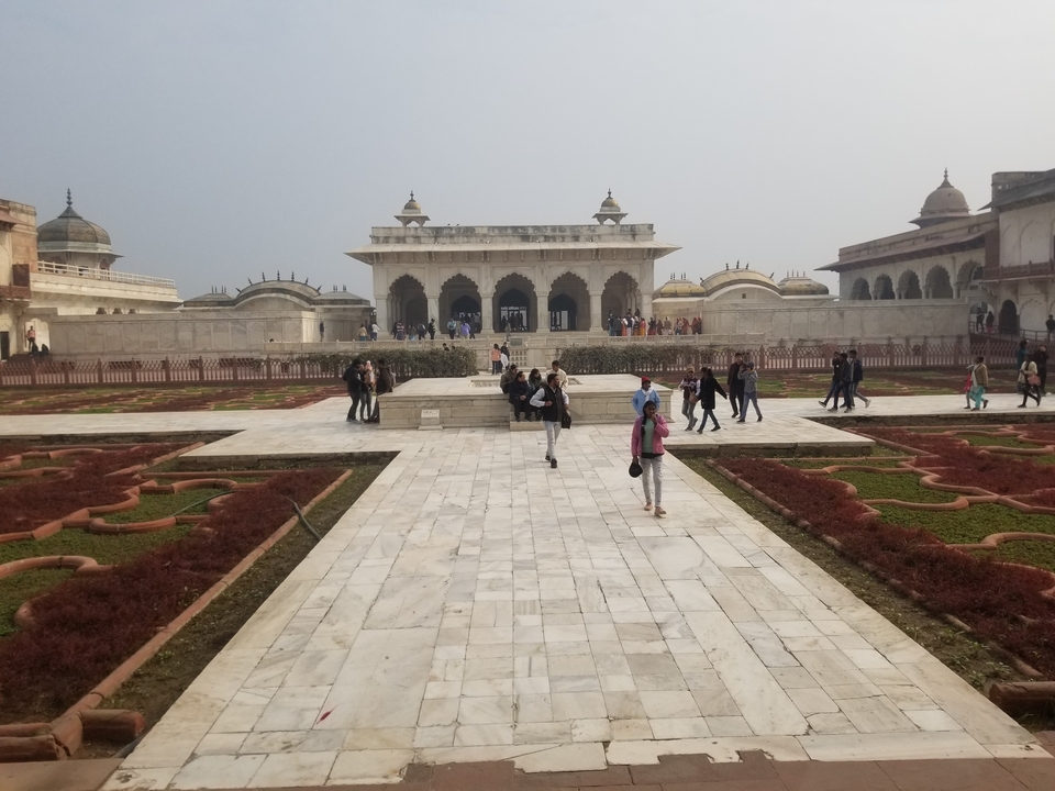 Des touristes se promènent dans un jardin bien entretenu avec une architecture historique en arrière-plan.