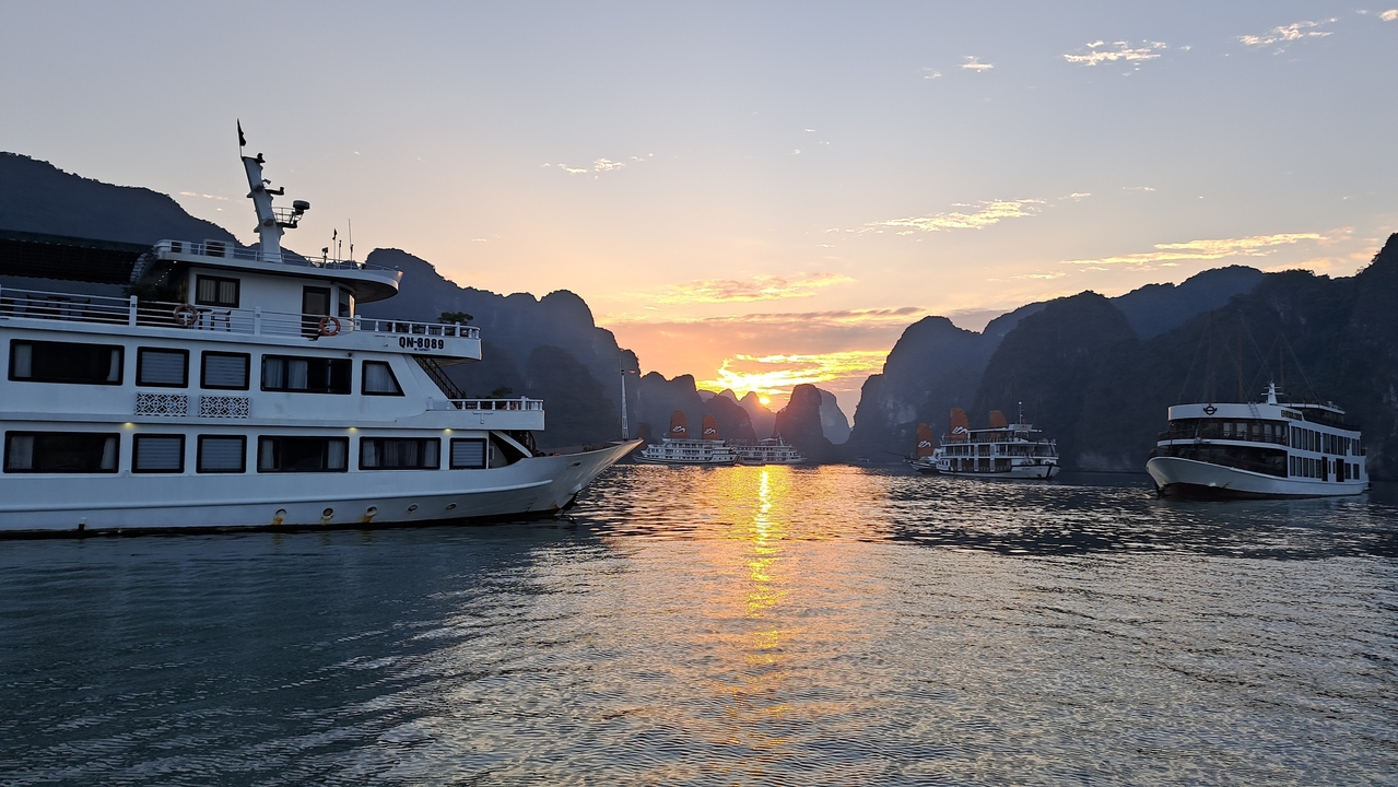 Bateaux sur la baie d'Halong au coucher du soleil avec un éclairage dramatique.