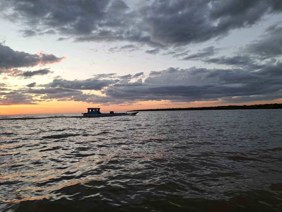 Un bateau sur une rivière sous un ciel de coucher de soleil dramatique.