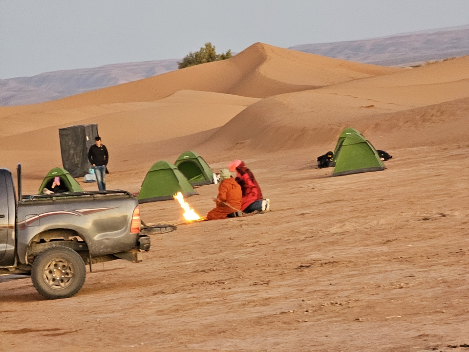 Des gens qui campent dans le désert avec des tentes et un feu de camp.