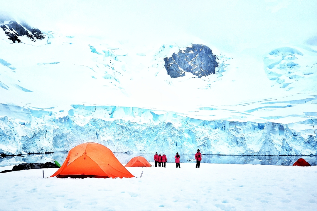 Des tentes orange dressées sur la neige avec en toile de fond des montagnes glacées et des glaciers.