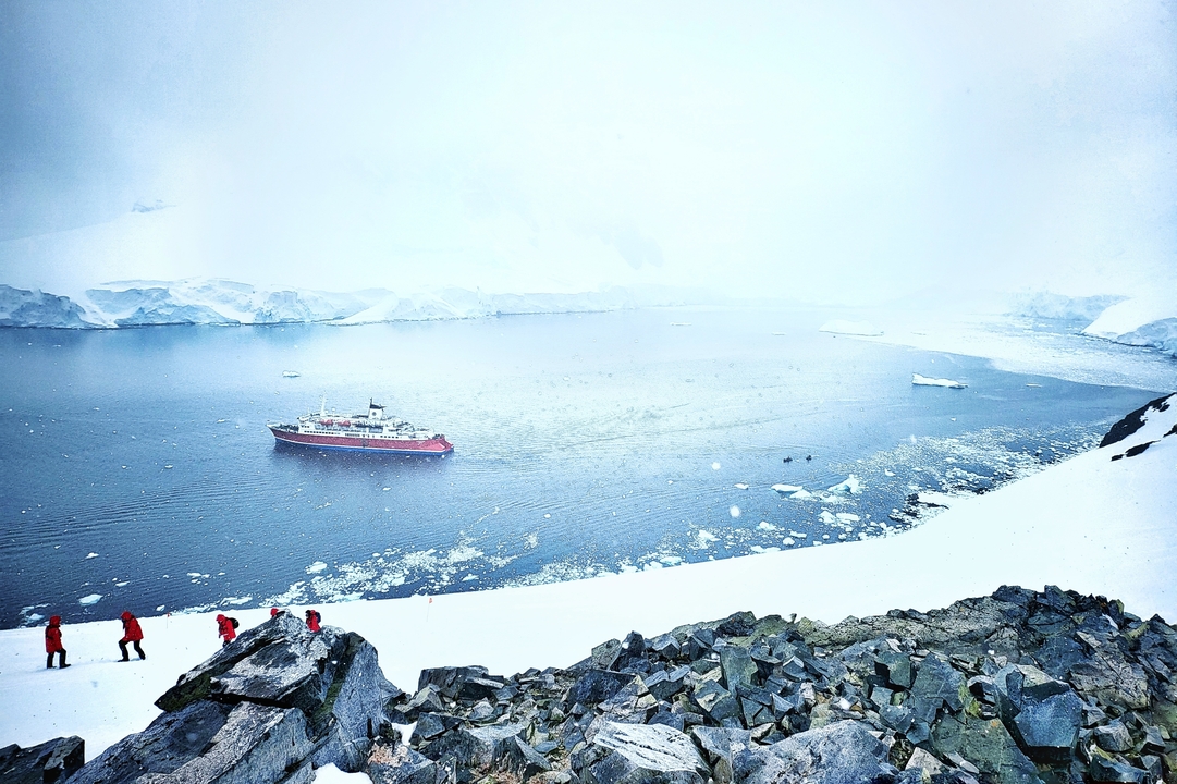 Des gens escaladant une pente enneigée surplombant une baie glacée avec un grand navire.