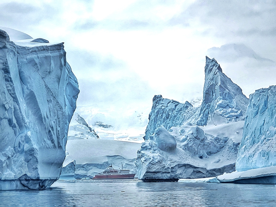 Majestueuses formations de glace avec un petit navire au loin.