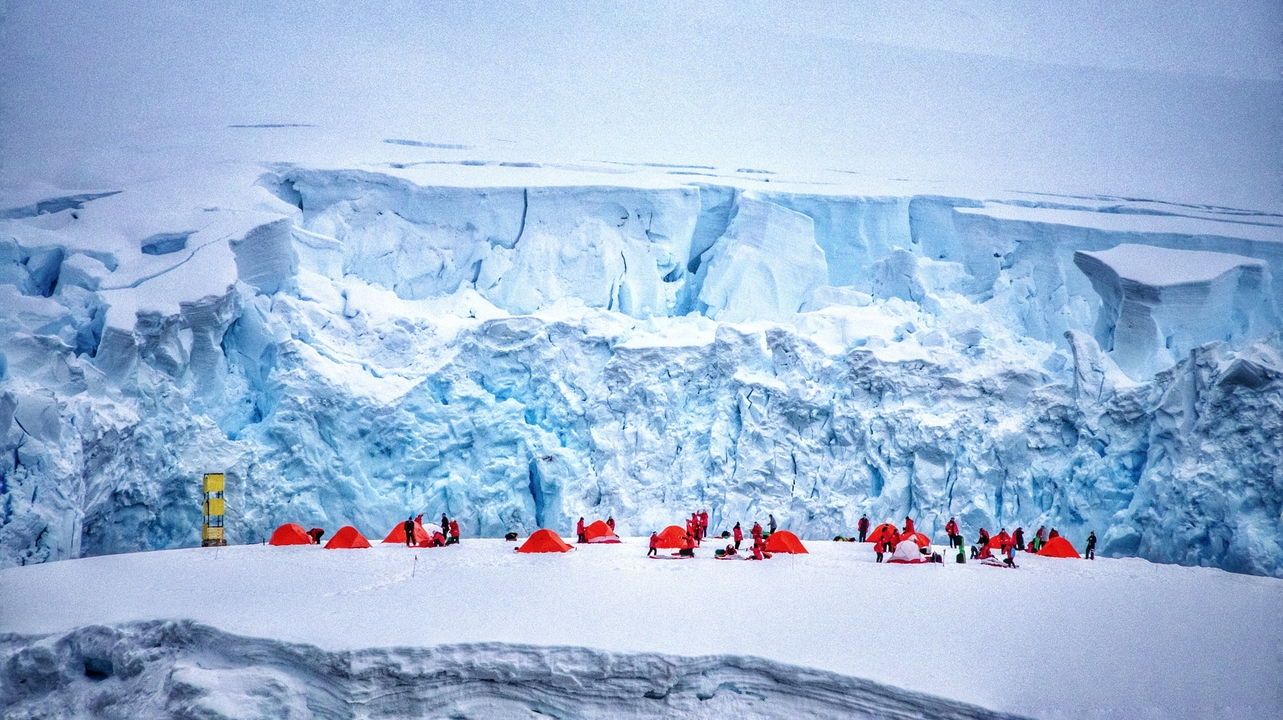 Camping sur un plateau enneigé avec des tentes rouge vif et un arrière-plan glacé.