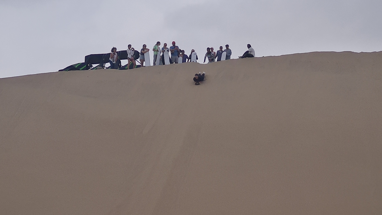 Des gens qui font du sandboard en descendant une grande dune de sable.