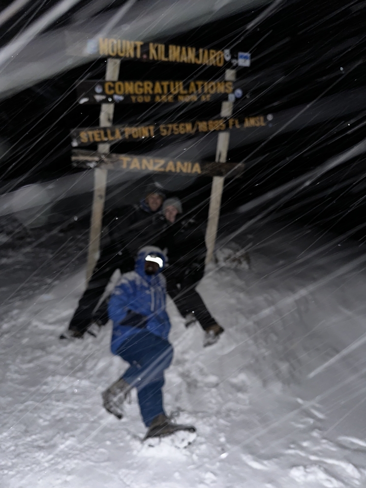 Image floue de nuit de personnes sous un panneau Tanzanie dans des conditions neigeuses.