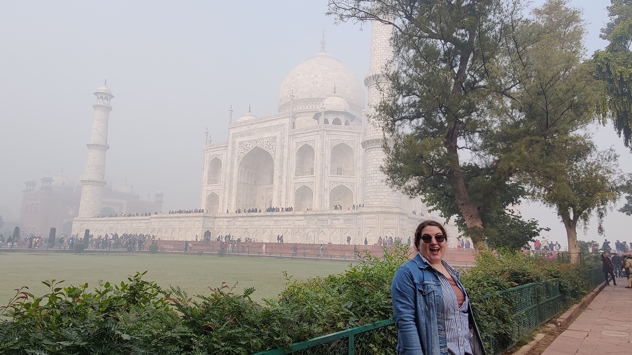 Femme souriante devant le Taj Mahal par une journée brumeuse.