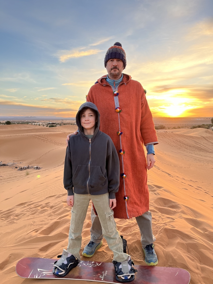 Une femme et un enfant debout sur des dunes de sable au coucher du soleil.