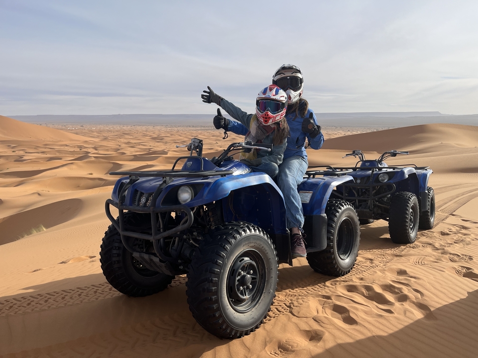 Deux personnes faisant du quad sur une dune de sable.