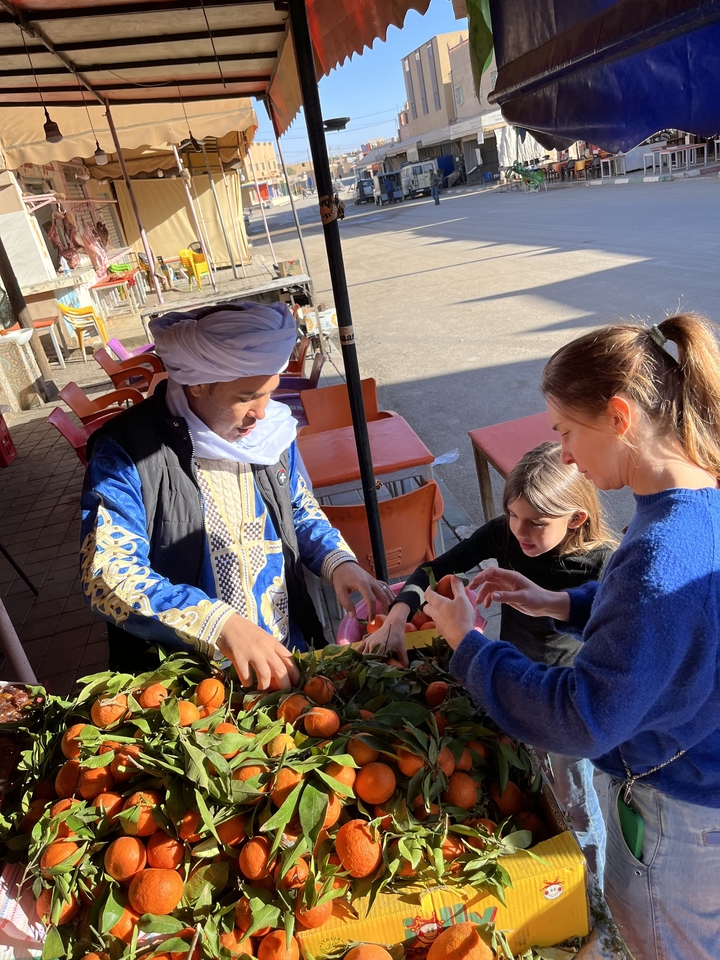 Deux personnes interagissant avec un vendeur local à côté d'un étalage de fruits.