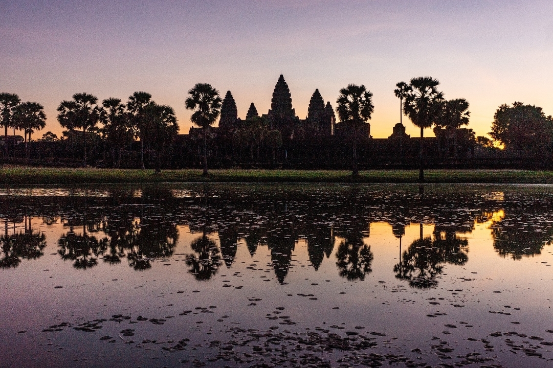 Silhouette d'Angkor Vat se reflétant dans l'eau au lever du soleil.