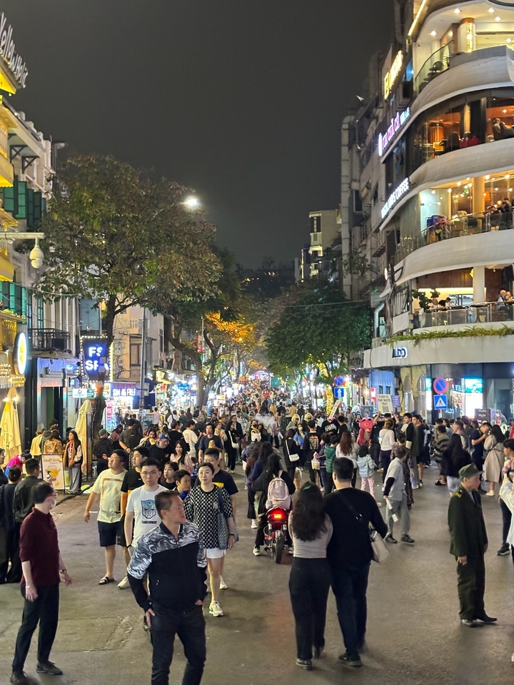 Une rue bondée de Hanoï grouillante de monde et illuminée de lumières éclatantes la nuit.