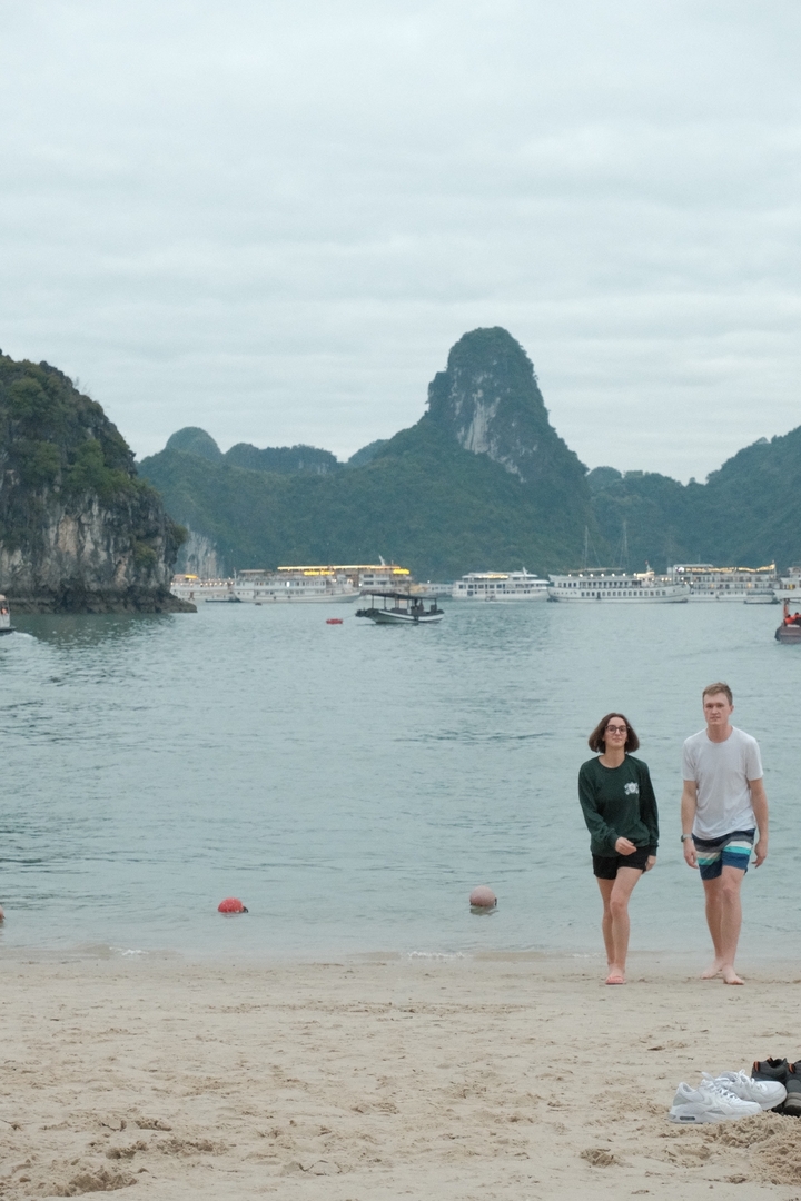 Deux personnes debout devant la baie d'Halong, avec des bateaux et des îles rocheuses en arrière-plan.
