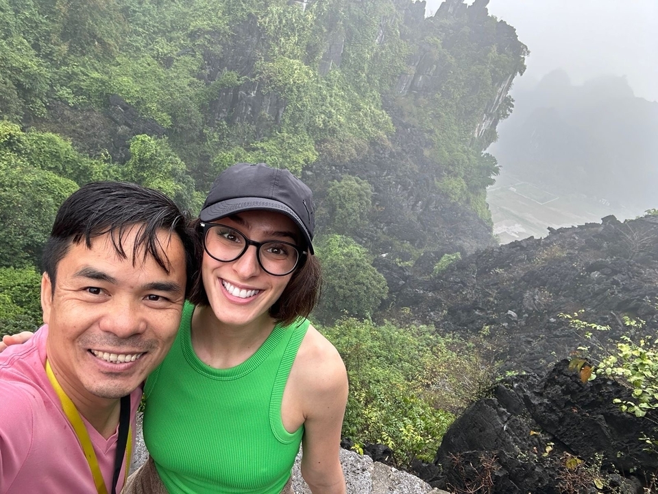 Deux personnes souriantes avec une vue panoramique de collines et de verdure en arrière-plan.