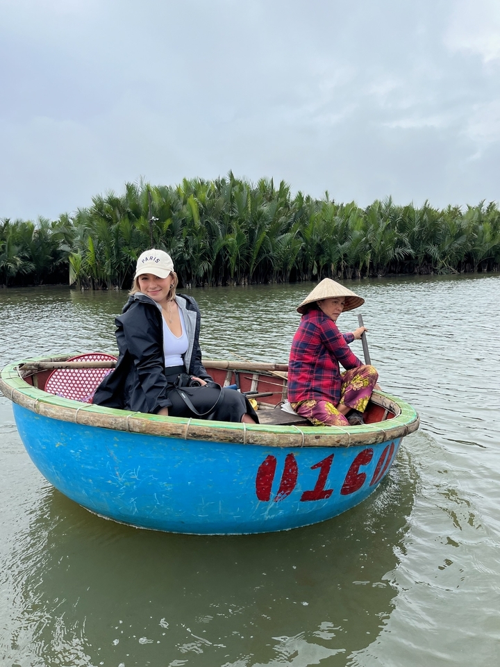 Deux personnes dans un petit bateau rond sur une rivière, avec des palmiers en arrière-plan.