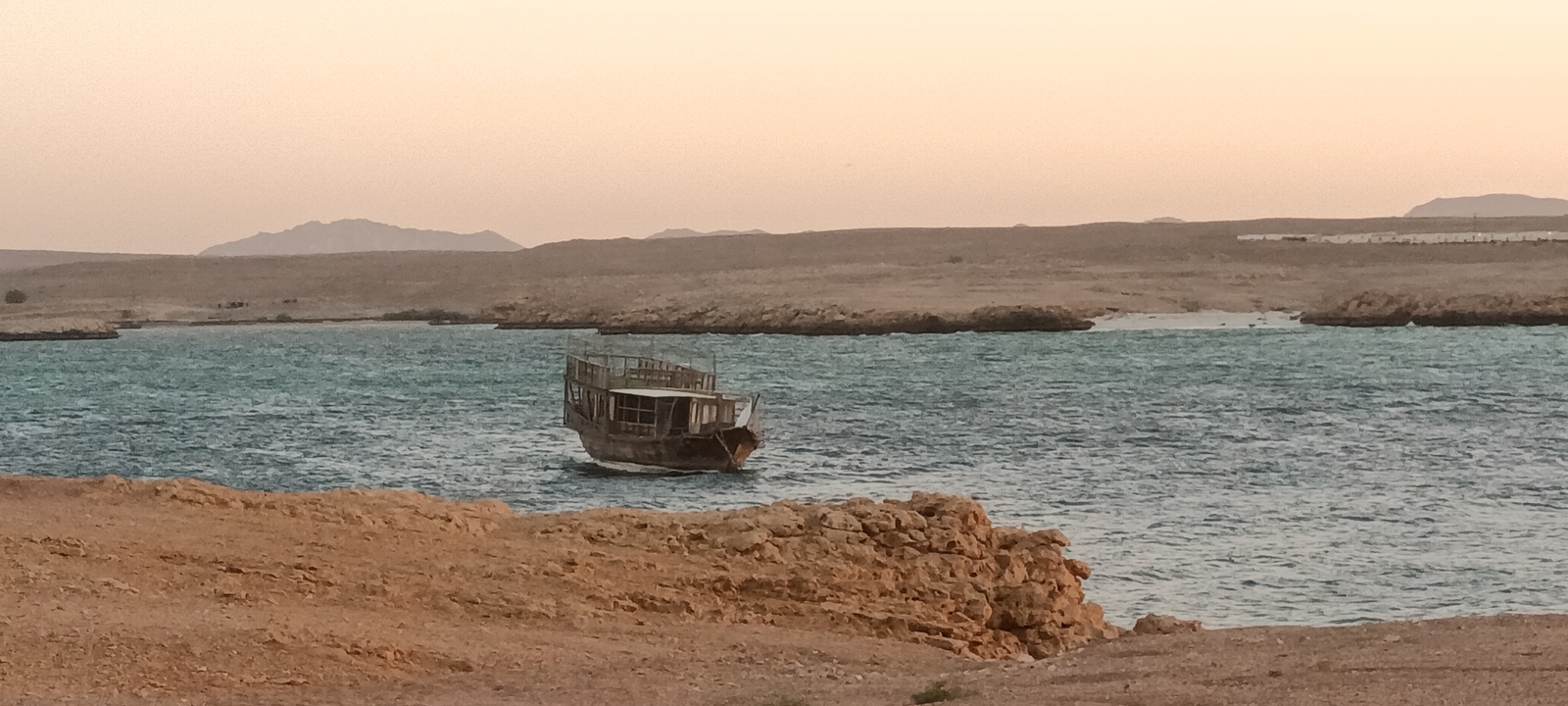 Vieux bateau en bois dans une étendue d'eau avec une rive rocheuse.