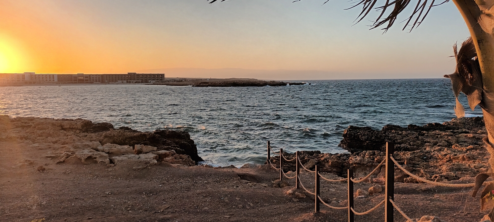 Coucher de soleil au bord de la mer avec des bâtiments au loin.